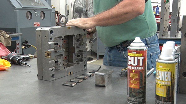 Two cans of Stoner Mold Cleaner sit on a workbench while a worker cleans a mold beside them.