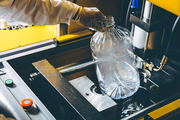 A worker pulls a plastic bottle out of a mold.