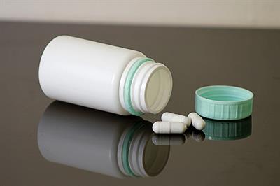 Open, white pill bottle with blue cap and pills spilling out